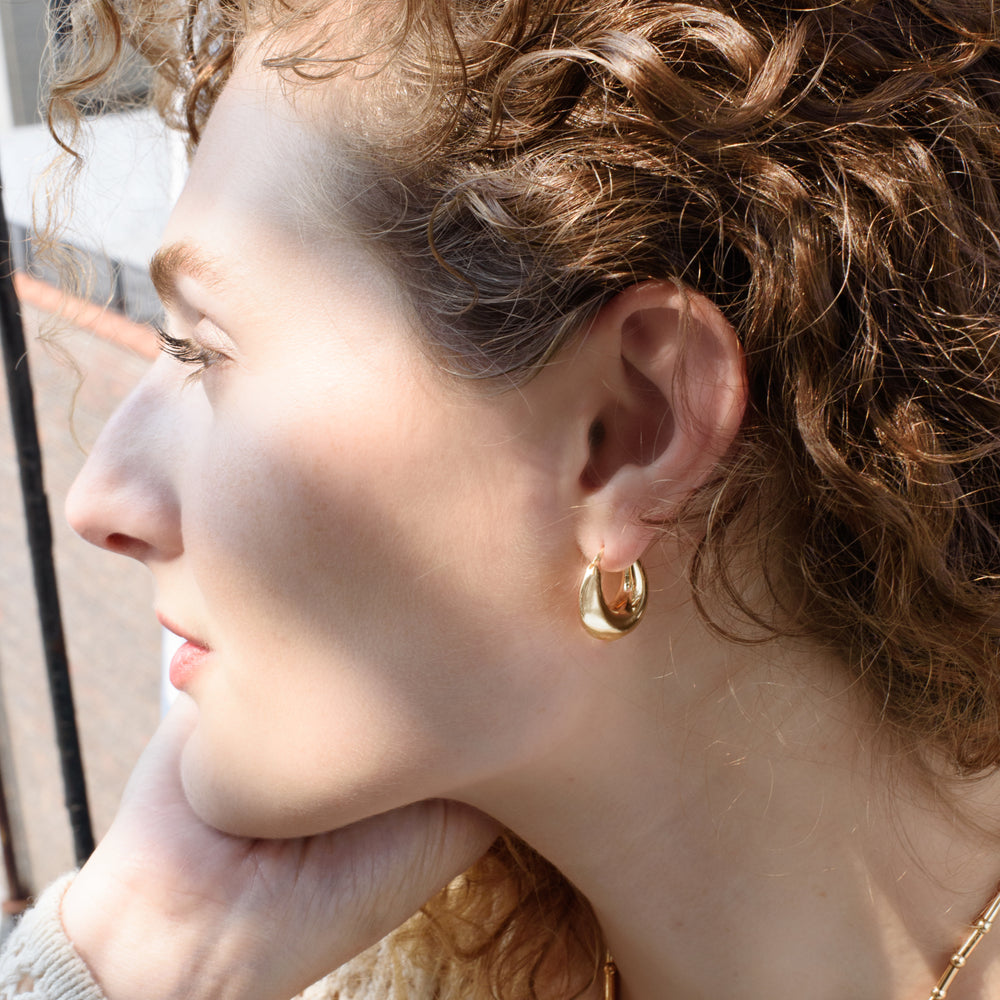 The Everri Day Huggies are a sleek and modern take on the classic hoop earring, inspired by the elegant curve of a half-moon. These solid, half-moon shaped earrings are meticulously crafted and plated with gold, representing balance and serenity. With a minimalist design that hugs the ear closely, they offer a chic look that seamlessly transitions from day to night, adding a subtle celestial charm to any outfit and celebrating personal evolution and style.