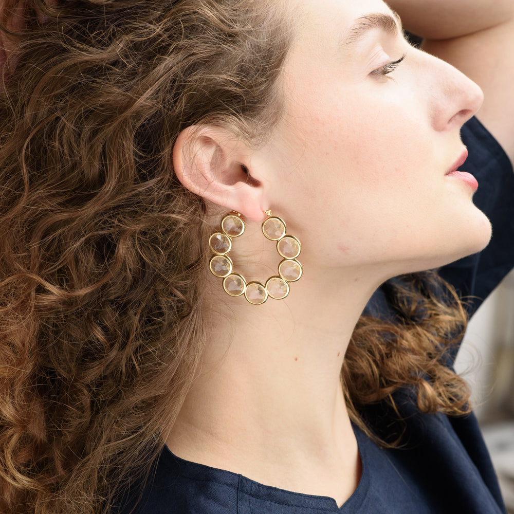 The Celestial Hoop Earrings showcase nine concentric circles crafted from brass and plated in radiant gold, symbolizing harmony and infinite possibilities. Each circle is intricately filled with faceted Diamond Essence, creating a mesmerizing effect with every movement. These elegant earrings are designed to celebrate personal growth and transformation, making them a bold statement piece for any occasion.