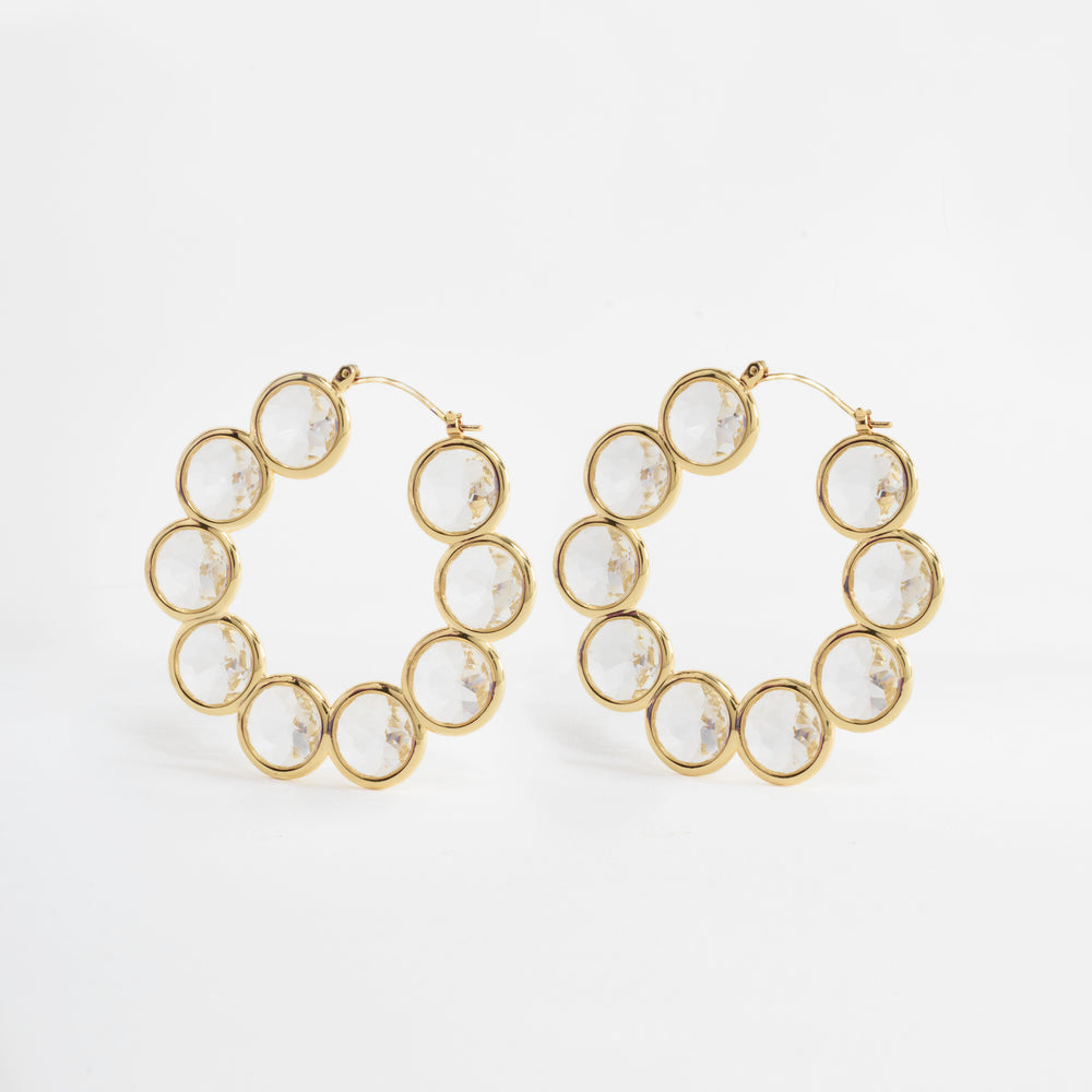 The Celestial Hoop Earrings showcase nine concentric circles crafted from brass and plated in radiant gold, symbolizing harmony and infinite possibilities. Each circle is intricately filled with faceted Diamond Essence, creating a mesmerizing effect with every movement. These elegant earrings are designed to celebrate personal growth and transformation, making them a bold statement piece for any occasion.