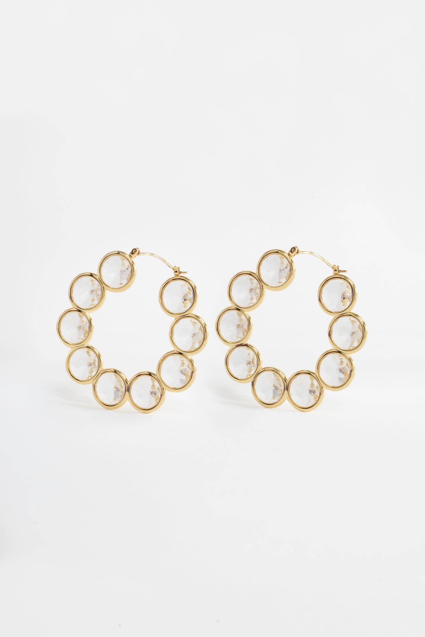 The Celestial Hoop Earrings showcase nine concentric circles crafted from brass and plated in radiant gold, symbolizing harmony and infinite possibilities. Each circle is intricately filled with faceted Diamond Essence, creating a mesmerizing effect with every movement. These elegant earrings are designed to celebrate personal growth and transformation, making them a bold statement piece for any occasion.